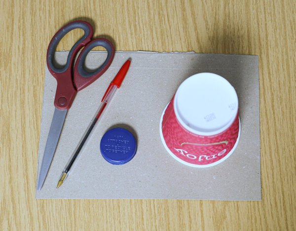 a pair of scissors, a pen, a bottle cap, a cup and a piece of card