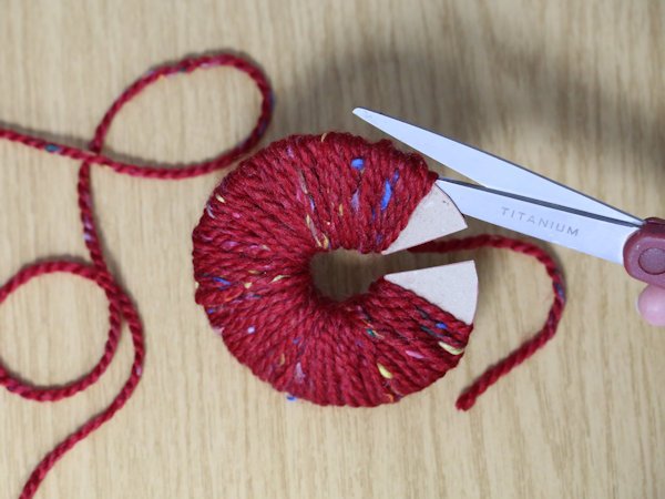 cutting through the outer of wool wrapped around two pieces of card