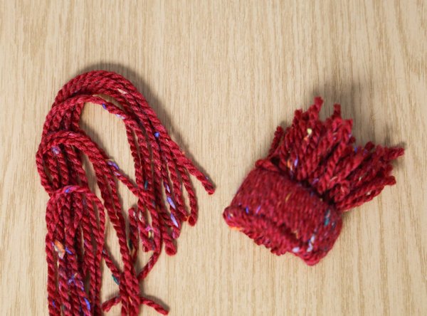 pushing the strands of wool through the cardboard tube to form the hat